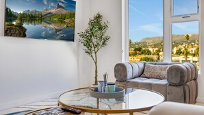 A modern living room with a glass coffee table, a sofa with cushions, a potted plant, and a framed landscape painting. - Luxury 3BR Hollywood Sign View by Oneluxstay (Los Angeles)