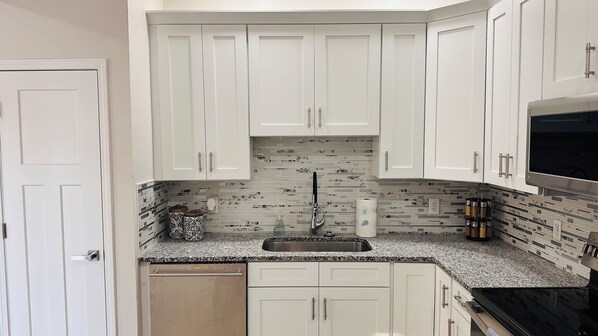 A modern kitchen with white cabinets, a granite countertop, and a stainless steel sink.