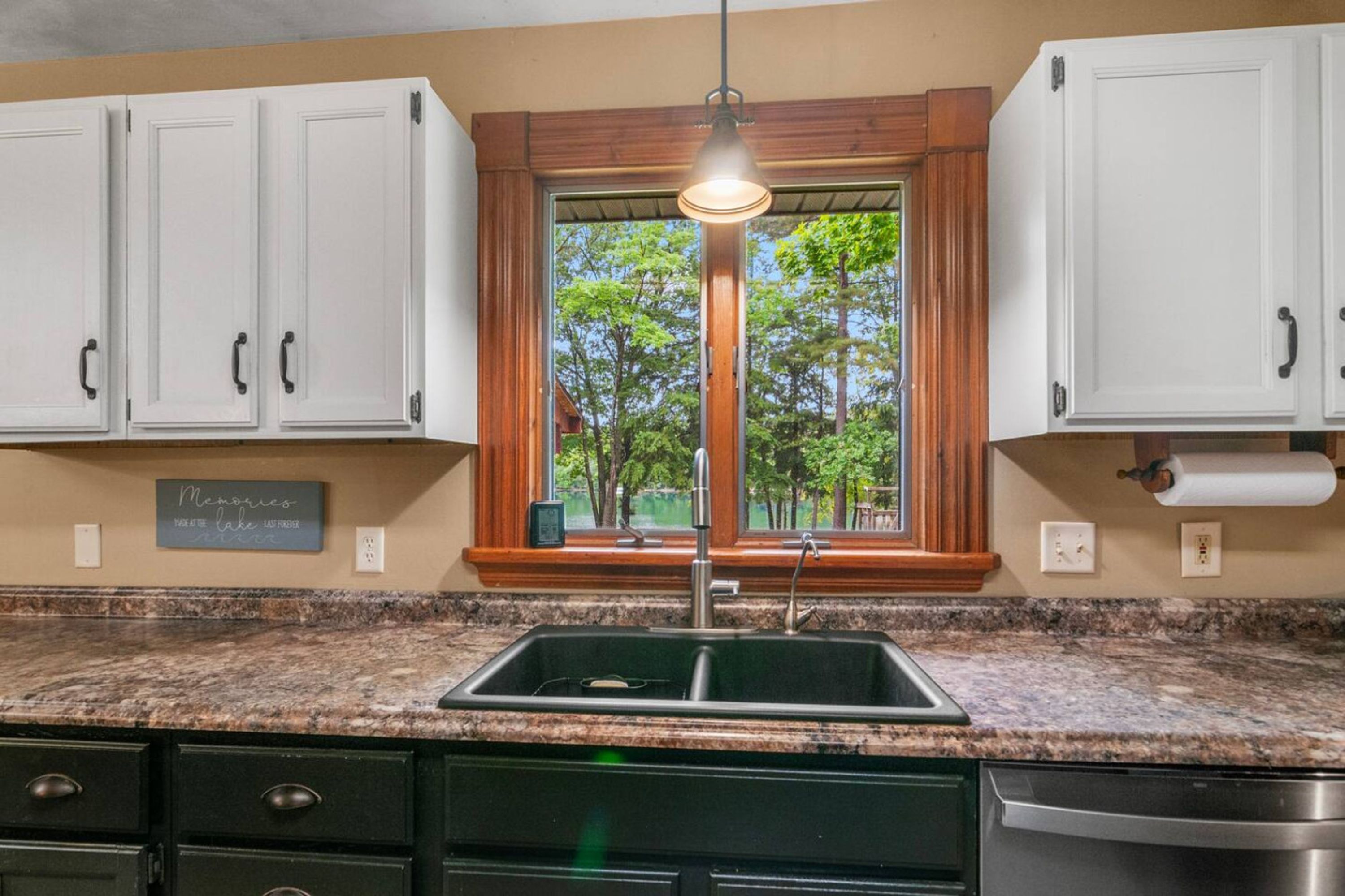 A kitchen with white cabinets, a granite countertop, a stainless steel sink, and a window with a view of trees.