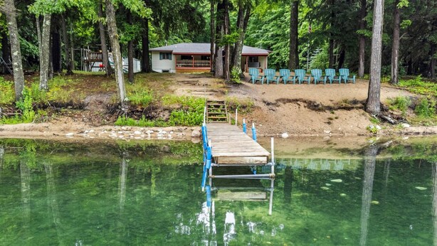 Muelles de madera que conducen a una casa con porche, rodeada de árboles y aguas cristalinas.
