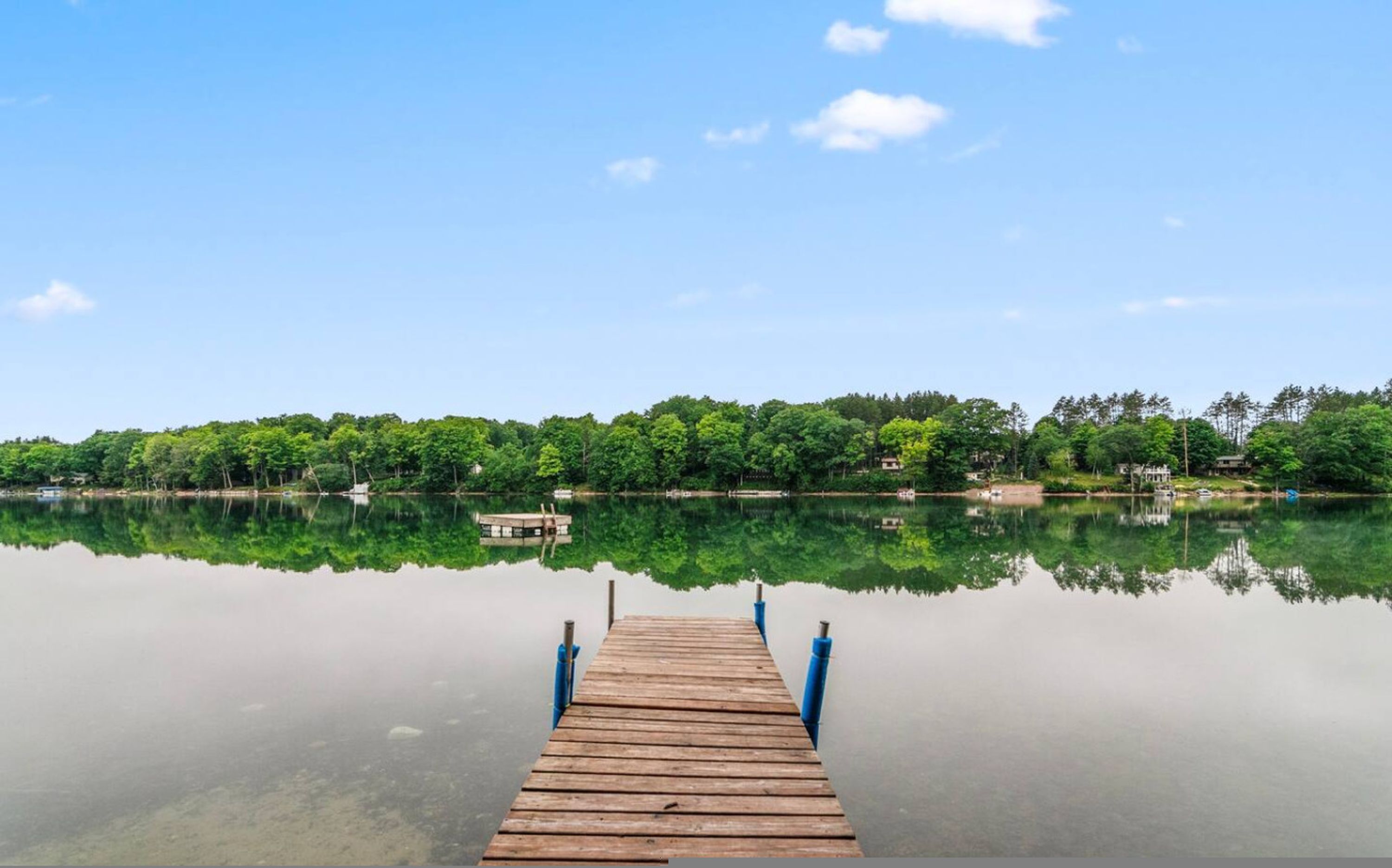 Een houten steiger die zich uitstrekt over kalm water, met een heldere weerspiegeling van bomen en lucht.