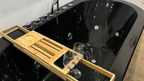 Une salle de bain moderne avec une baignoire noire, un plateau en bois et deux verres.