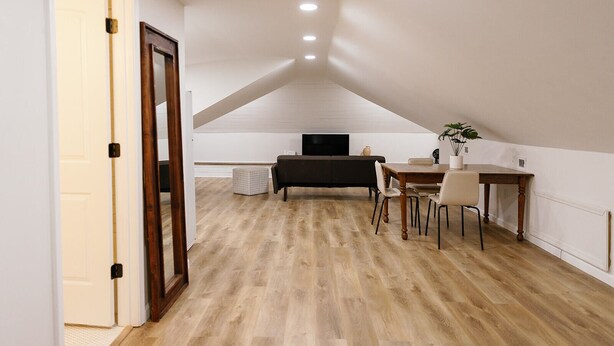 Een kamer met een houten vloer, een eettafel met stoelen, een bank en een televisie.