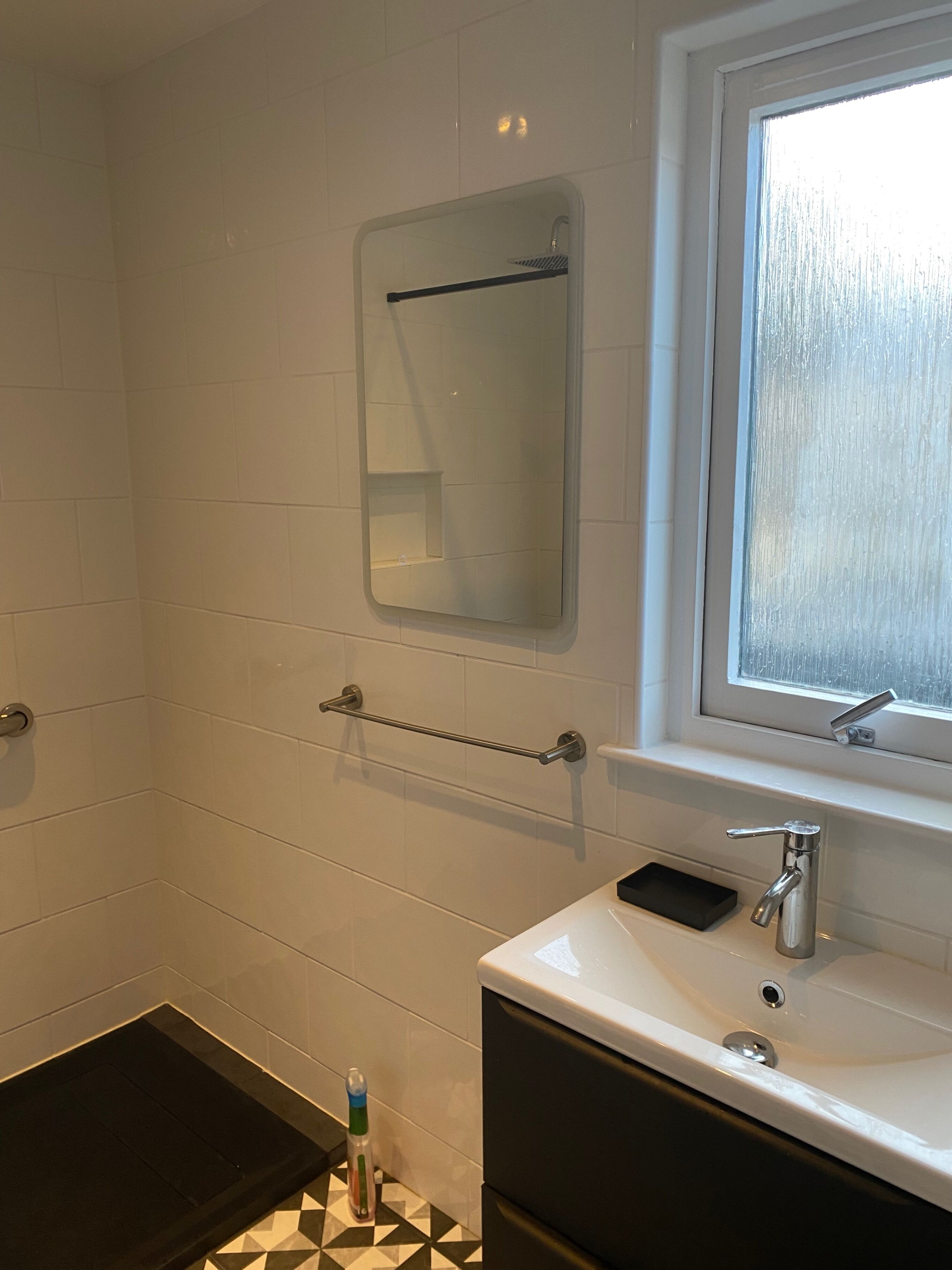 A bathroom with white tiled walls, a mirror, a window, a sink, and a towel rack.