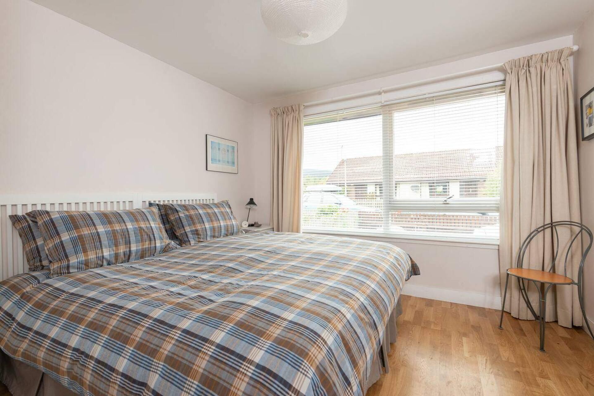 A bedroom with a bed, a window with curtains, a chair, and a picture on the wall.
