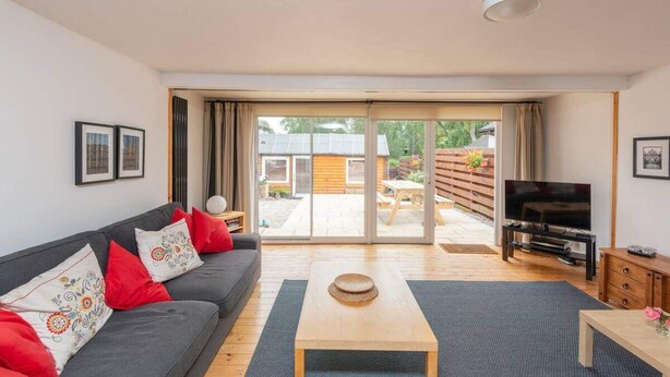 A living room with a sofa, a coffee table, a TV, and a sliding glass door leading to an outdoor area. - 4guests-2br-privategarden-freeparking (Aviemore)