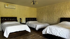 Ein Hotelzimmer mit zwei Einzelbetten, Holzboden, einer wandmontierten Klimaanlage und einem schlichten Kronleuchter.