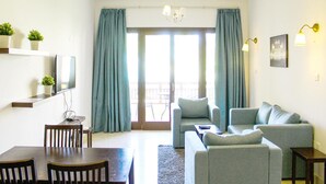 En moderne stue med sofaarrangement, spisebord med stole, lysekrone og balkon med gardiner.