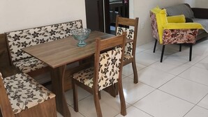 A dining area with a wooden table and floral-patterned chairs, a sofa with a floral cushion, and a tiled floor. - Apartment in Peroba/Maragogi (Barra Grande)