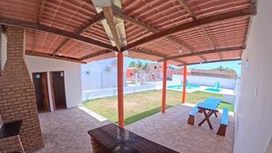 A covered outdoor area with a brick wall, a counter, and a pool in the background. - Apartment in Peroba/Maragogi (Barra Grande)