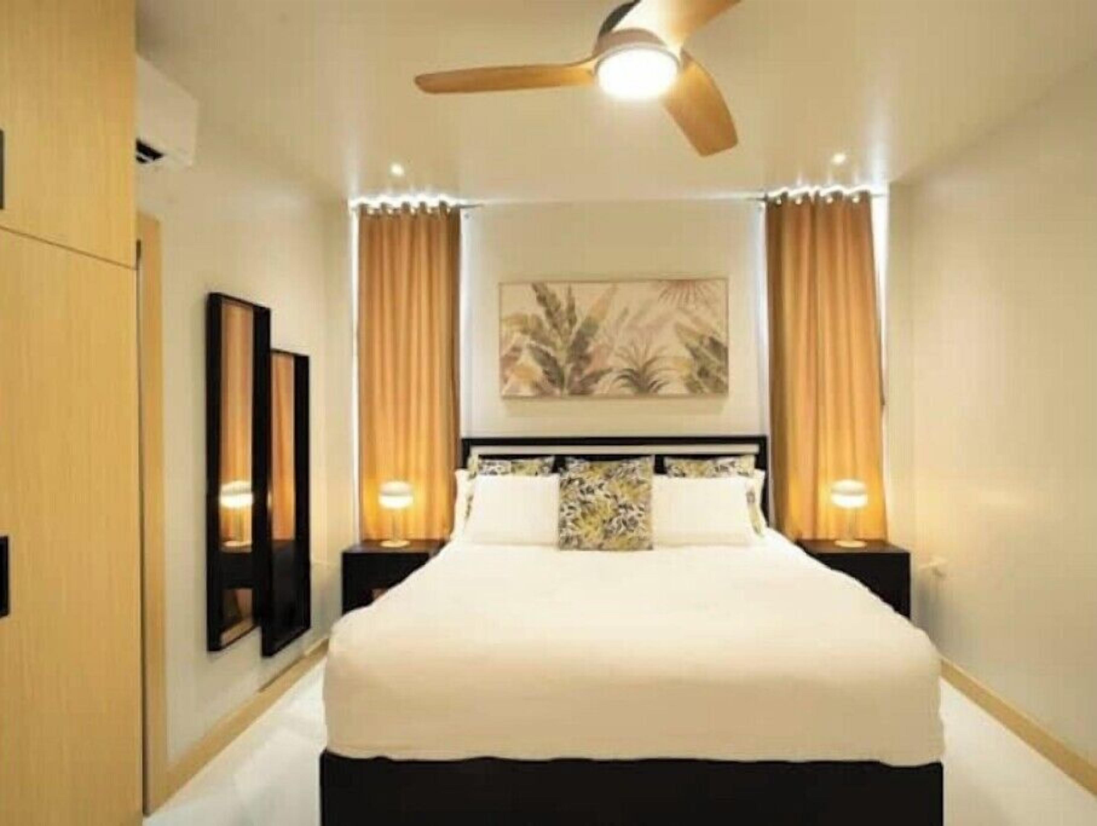 A hotel room with a large bed, a ceiling fan, two bedside lamps, and a painting on the wall.