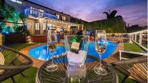 An outdoor pool area with lounge chairs, a table with a bottle of champagne, and glasses of wine. - The Fairway Retreat at Vista del Verde (San Diego)