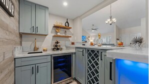 A modern kitchen with light blue cabinets, a wine cooler, and a bar area with a blue light. - The Fairway Retreat at Vista del Verde (San Diego)