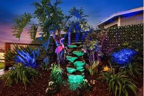 A garden with a rock waterfall, tropical plants, and a flamingo statue.