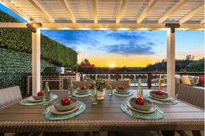 An outdoor dining area with a view of the sunset, a pool, and a pergola.