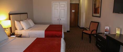 A hotel room with two beds, a desk, a chair, and a television.