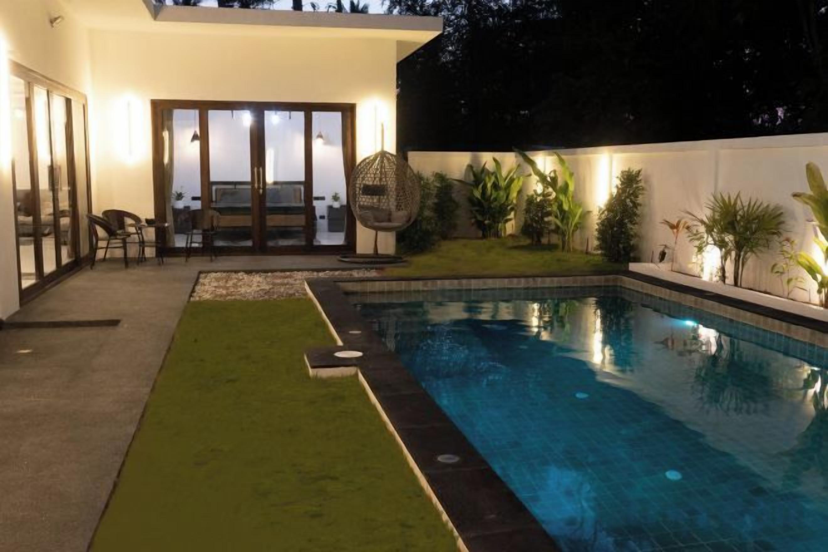 A swimming pool with a grassy area and a patio with chairs and a table.
