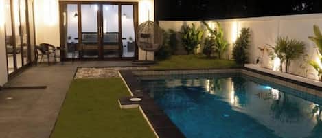 Una piscina con césped, un patio amueblado con sillas y una mesa.