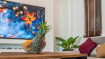 A living room with a flat-screen TV, a wooden table, a pineapple, and a plant.