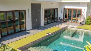 A modern outdoor swimming pool with glass doors, a seating area, and a small garden. - Ozzy Villa Phangan (Koh Phangan)
