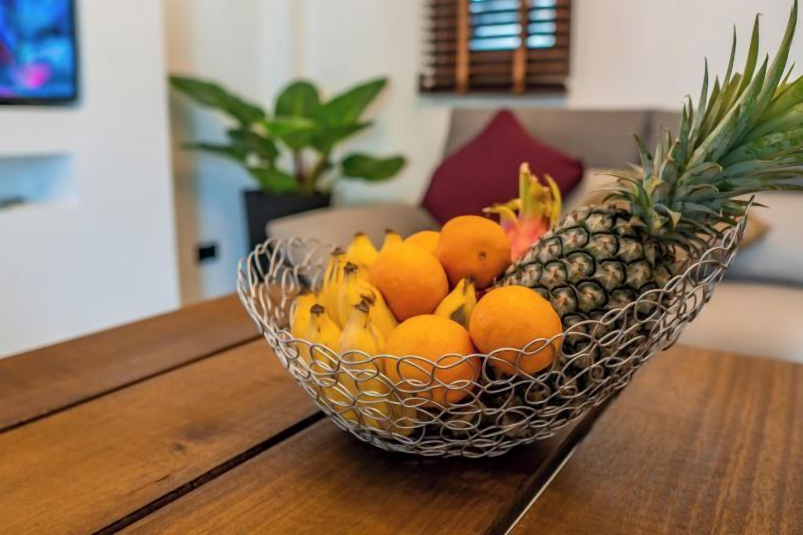 Un panier en fil métallique contenant des oranges et un ananas, posé sur une table en bois.