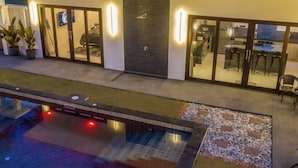 A modern building with a swimming pool, a patio area, and a well-lit entrance. - Ozzy Villa Phangan (Koh Phangan)
