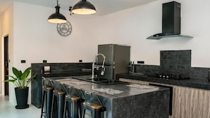 A modern kitchen with a central island, bar stools, pendant lighting, and a built-in stove. - Ozzy Villa Phangan (Koh Phangan)