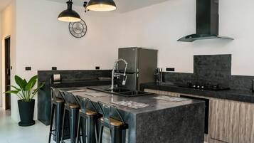 A modern kitchen with a central island, bar stools, a refrigerator, and pendant lighting.