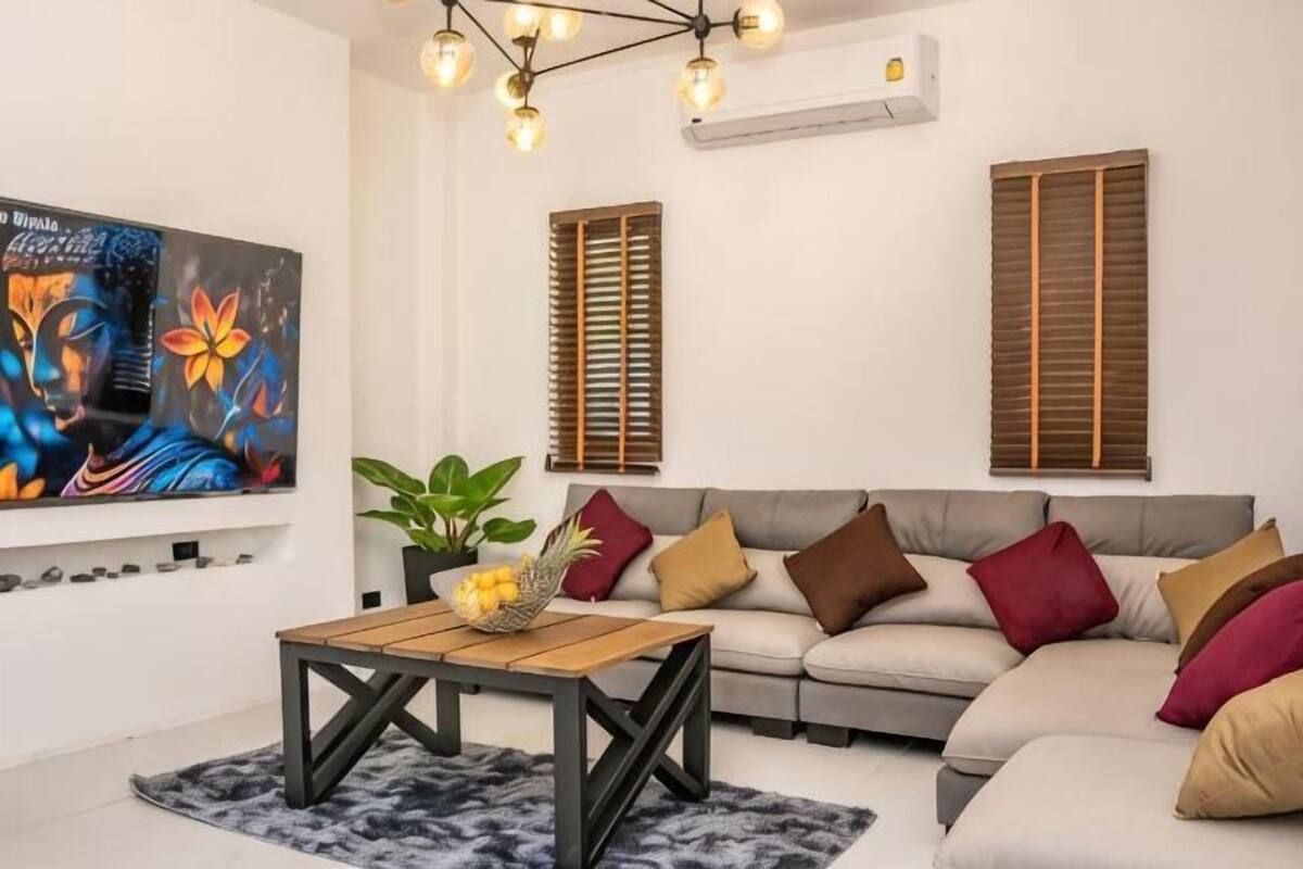 A living room with a sofa, a coffee table, a painting, and a ceiling light fixture.