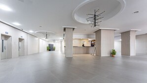 Un amplio vestíbulo con una mesa de recepción, grandes columnas y un candelabro moderno.