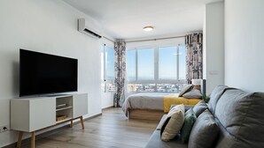 Una sala de estar moderna con una televisión de pantalla plana, un sofá, una cama y un ventanal con vistas a la ciudad.