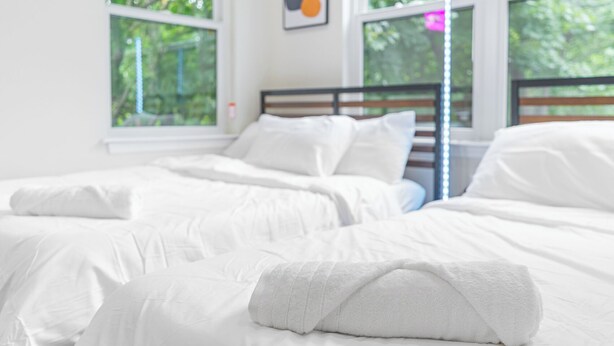 Ein Hotelzimmer mit zwei Betten, weißer Bettwäsche und großen Fenstern mit Blick auf Grünflächen.