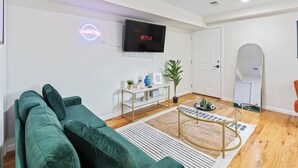 Ein modernes Wohnzimmer mit einem grünen Sofa, einem an der Wand montierten Fernseher, einem kleinen Tisch mit Pflanzen und einem Spiegel.
