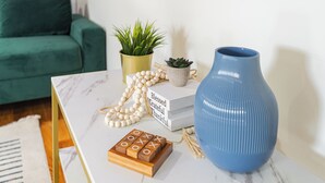 Ein Marmortisch mit einer blauen Vase, einer weißen Perlenkette, einer kleinen Pflanze und einem hölzernen Spielbrett.