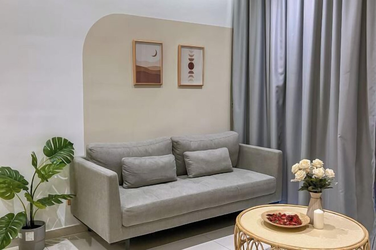 A living room with a grey sofa, a round coffee table, a potted plant, and a vase with white flowers.