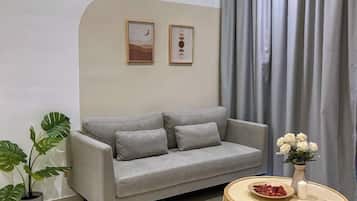 A living room with a grey sofa, a round coffee table, a potted plant, and a vase with white flowers.