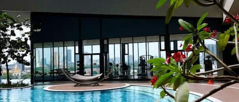 Piscina interior con vistas a la ciudad a través de grandes ventanales, zona de estar con una hamaca y un espacio de asientos circular.