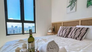 A hotel room with a bed, a window with a city view, a bottle of wine, and a tray with a candle and flowers. - Kenwingston Skyloft Apartment Doorsteps to Brt Subang USJ (Subang Jaya)