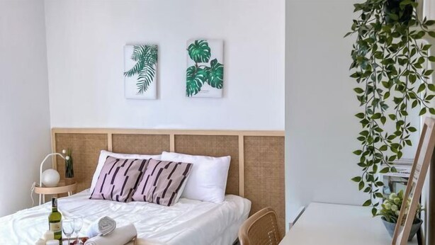 A neatly made bed with a tray of toiletries, a bottle of wine, and glasses. There are two framed botanical prints on the wall above the bed. - Kenwingston Skyloft Apartment Doorsteps to Brt Subang USJ (Subang Jaya)