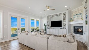 A spacious living room with a large sectional sofa, a flat-screen TV, and a fireplace. - Featured in American Dream Home !  Stunning Oceanfront Views for Days !! (Galveston)