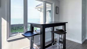 Una habitación con un ventanal grande con vistas al mar, una mesa de madera oscura con dos taburetes de bar y un cuadro en la pared.