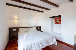 A bedroom with a bed, wooden beams, two wall-mounted lights, and a small picture frame.