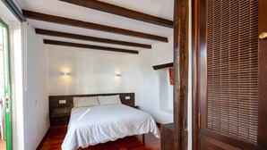 Quarto com cama, vigas de madeira, janela e porta com puxador.