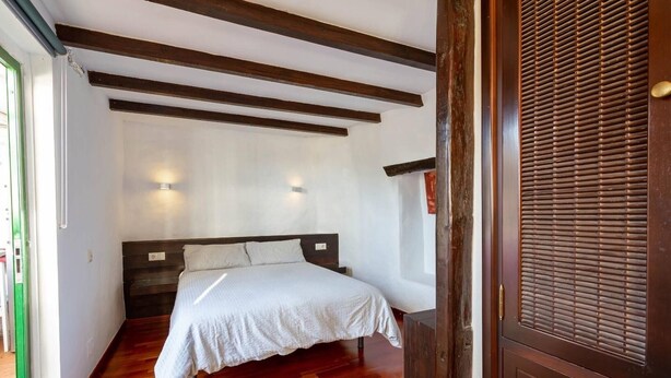 A bedroom with a bed, wooden beams, a window, and a door with a handle.