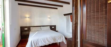 A bedroom with a bed, wooden beams, a window, and a door with a handle.