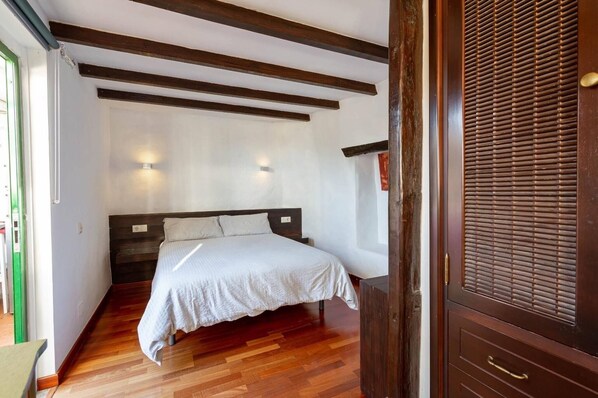 A bedroom with a bed, wooden beams, a window, and a door with a handle.