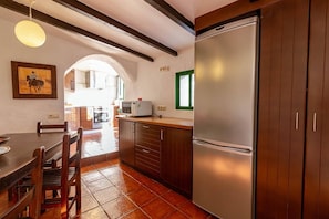 A kitchen with a refrigerator, microwave, wooden cabinets, and a dining table with chairs.