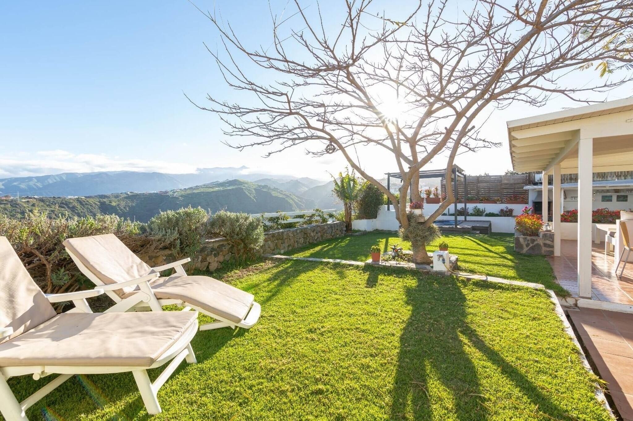Un césped cuidado con un árbol, un patio con sillas y vistas a montañas distantes.
