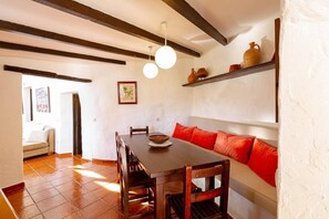 A dining area with a wooden table, chairs, a bowl, and a sofa with red cushions.