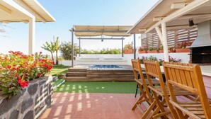 A patio with a hot tub, wooden chairs, a pergola, and potted plants.